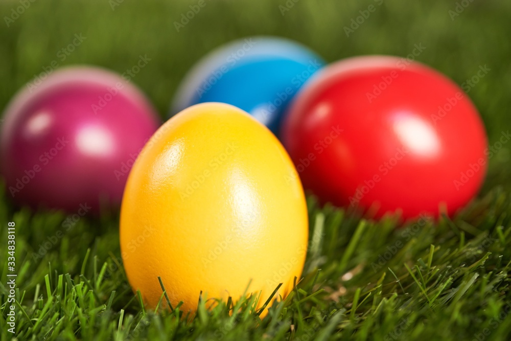 Close up image of traditional, yellow, painted easter egg in green grass with colorful eggs in the background. Easter background. Close up of colorful easter eggs in grass. Easter background .