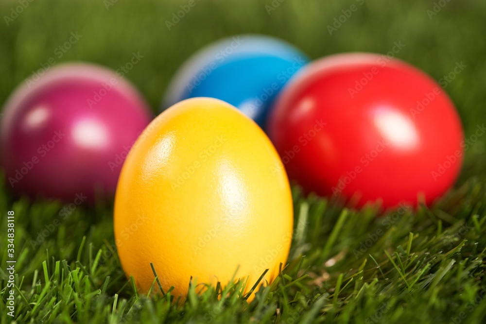 Close up image of traditional, yellow, painted easter egg in green grass with colorful eggs in the background. Easter background. Close up of colorful easter eggs in grass. Easter background . Close up image of traditional, yellow, painted easter egg in green grass with colorful eggs in the background. Easter background. Close up of colorful easter eggs in grass. Easter background .