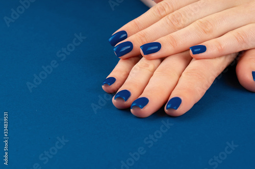 Female hands with manicure of classic blue color on blue background. Close up
