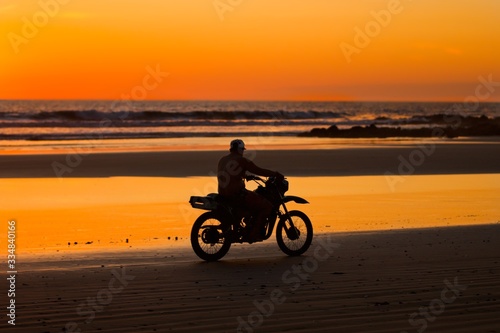 man riding a motorcycle on the beach at sunset