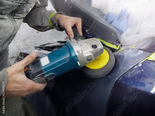cheerful, young man with glasses polishes, primes and paints a car in the garage