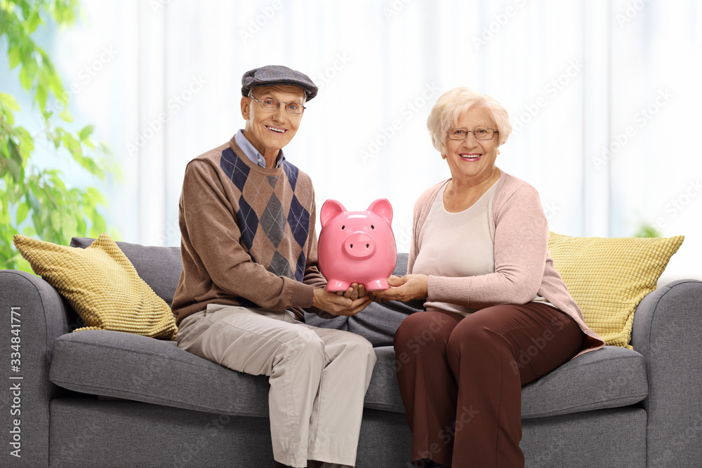 Elderly couple on a sofa at home holding a piggy bank