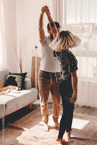 Happy couple is dancing in living room. Self isolation at home. Stay home. Entertain yourself quarantine coronavirus covid-19. Be happy together. Lifestyle apartment. Lots of light. Modern living room