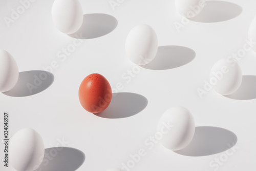 one brown egg among several white eggs on a white background