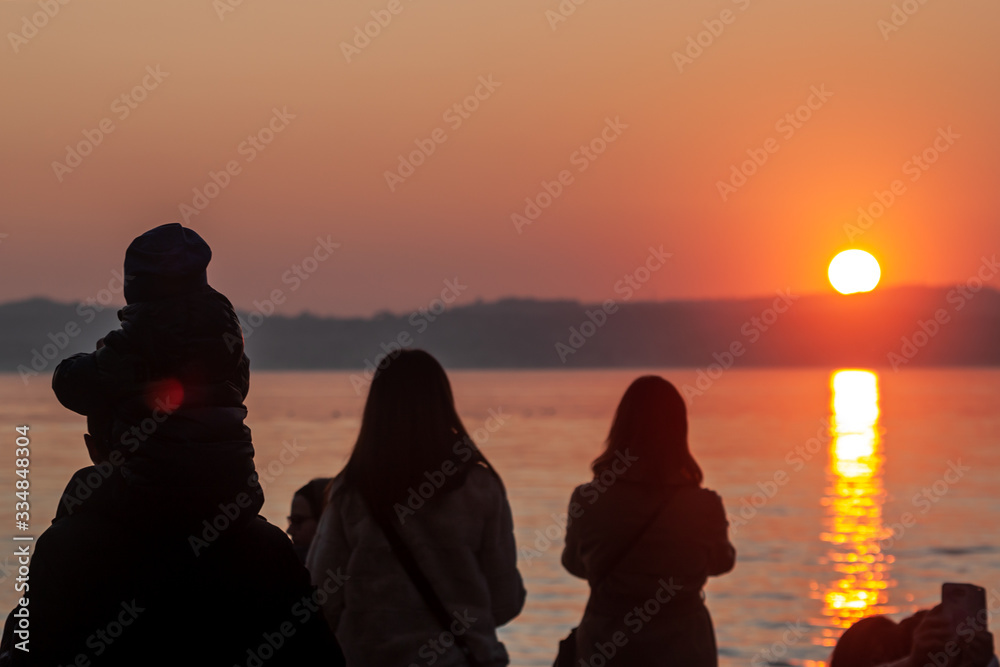 people silhouettes watching sunset over the lake