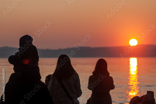 people silhouettes watching sunset over the lake