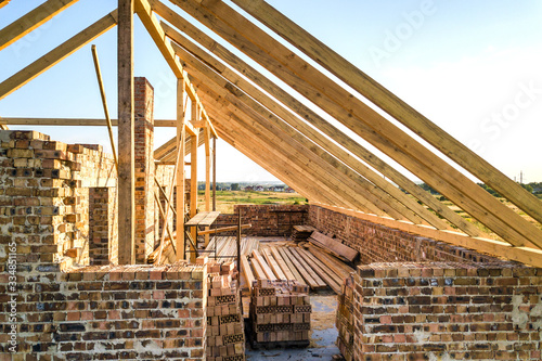 Unfinished brick house with wooden roof structure under construction. © bilanol