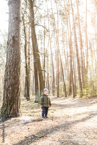 Toddler boy stands in the sunny forest