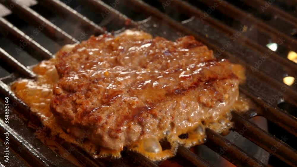 Beef cutlet for a burger is pressed with a spatula to the grill. Ingredients for hamburger preparation on the table. Beef cutlet for a burger is pressed with a spatula to the grill. Ingredients for hamburger preparation on the table.