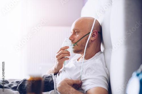 Man breathing through oxygen mask in bed. Covid-19 patient.