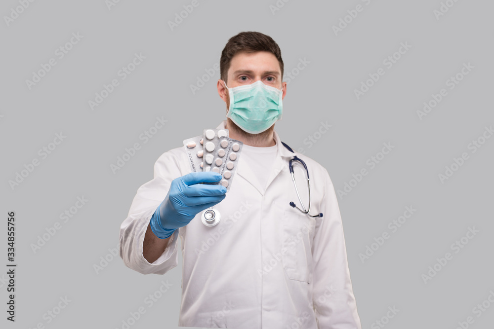 Man Doctor Showing Pills Wearing Medical Mask. Doctor Holding Tablets. Corona Virus Concept.