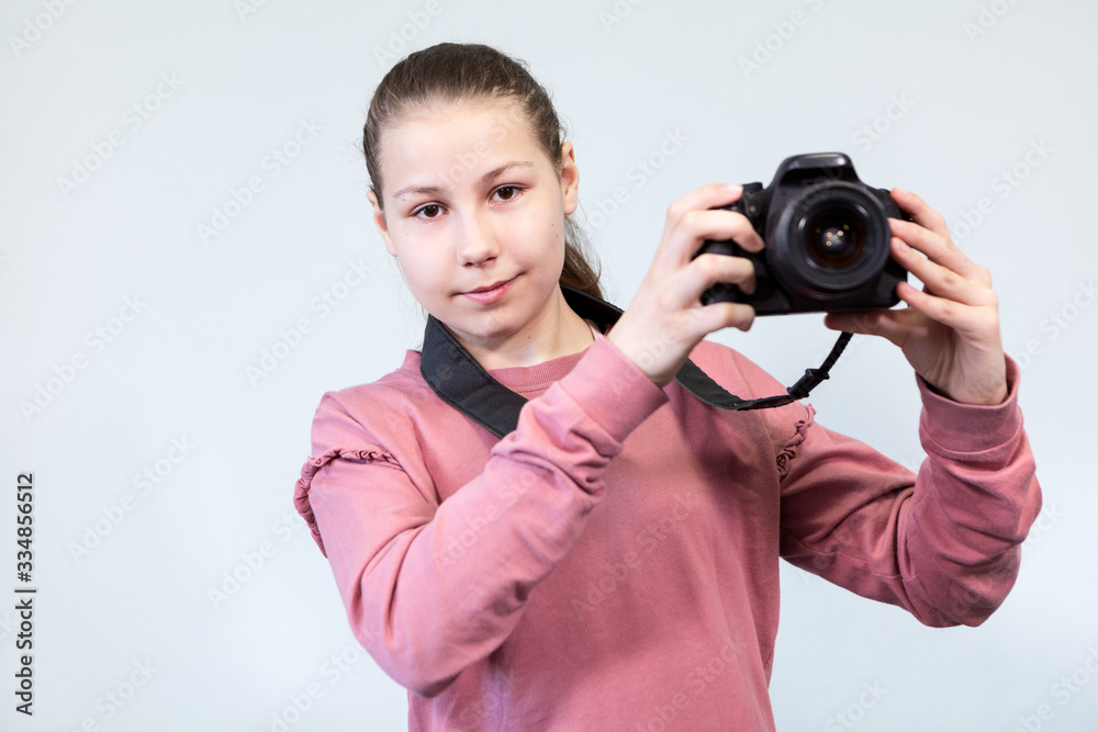 Portrait of teenage girl holding DSLR camera in hands, grey background, copyspace Portrait of teenage girl holding DSLR camera in hands, grey background, copyspace