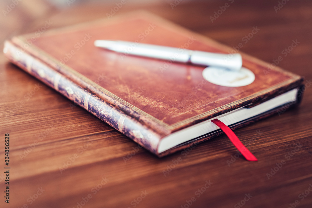 Antique brown notebook on wooden table with white pen, selective focus Antique brown notebook on wooden table with white pen, selective focus