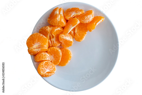 Top down view of pealed mandarin peaces on white plate on white background