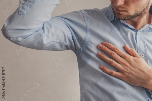 Man with hyperhidrosis sweating very badly under armpit in blue shirt, on grey. photo