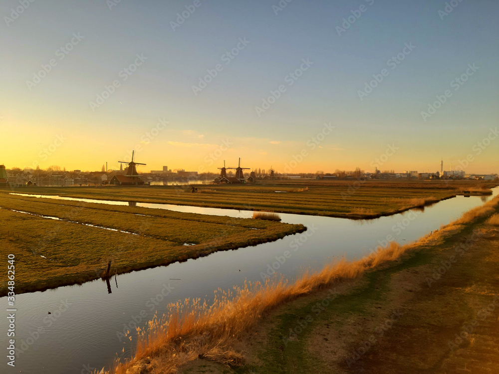 romantic Dutch countryside amidst extensive grassy meadows and canals whose water reflects the sunset