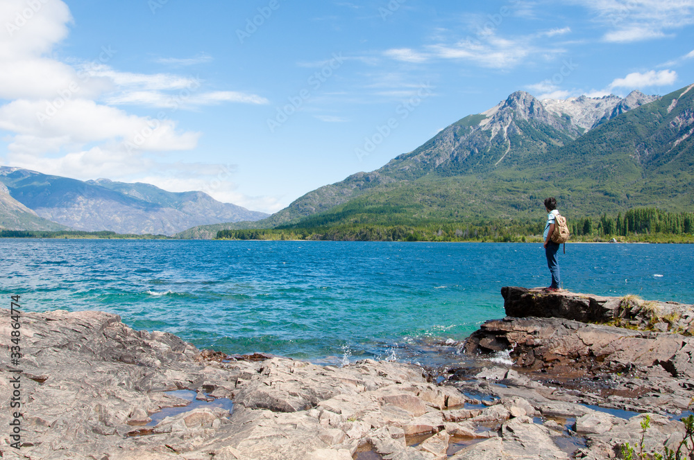 A man with a brown backpack standing and looking the mountains at the shore of Epuyen Lake. Photo taken at the Epuyen Provincial Park in the Cushamen department, Chubut province, Argentina. A man with a brown backpack standing and looking the mountains at the shore of Epuyen Lake. Photo taken at the Epuyen Provincial Park in the Cushamen department, Chubut province, Argentina.
