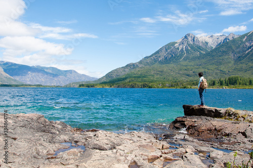 A man with a brown backpack standing and looking the mountains at the shore of Epuyen Lake. Photo taken at the Epuyen Provincial Park in the Cushamen department,  Chubut province, Argentina.