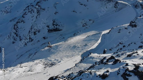 Orbit aerial over winter snowy mountain top ski tracks resort with skier people skiing. Drone video footage of Gondola lift cabin of ski-lift in the ski resort Val Thorens. photo