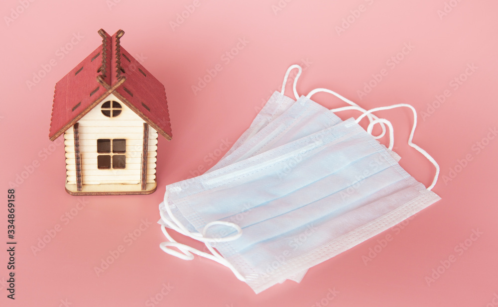 Toy house and medical masks for protection against coronavirus on a pink background