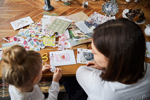 Happy mom and daughter sitting in the old style kitchen and doing scrapbooking