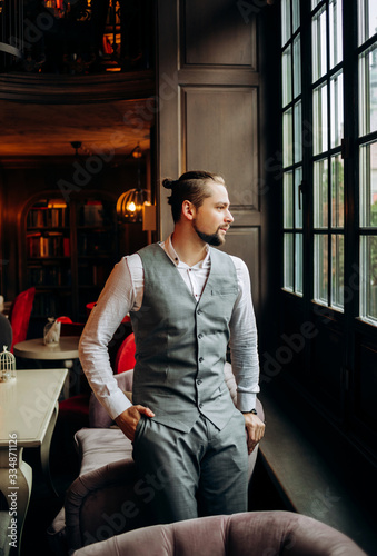 Stylish man with a beard in a graceful suit looks out the window.