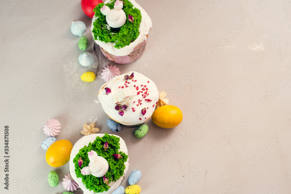 Orthodox Easter cakes decorated with cream in the form of grass and rabbit figurines made of white chocolate on a gray background next to painted eggs. Easter food concept. Idea for kids Orthodox Easter cakes decorated with cream in the form of grass and rabbit figurines made of white chocolate on a gray background next to painted eggs. Easter food concept. Idea for kids