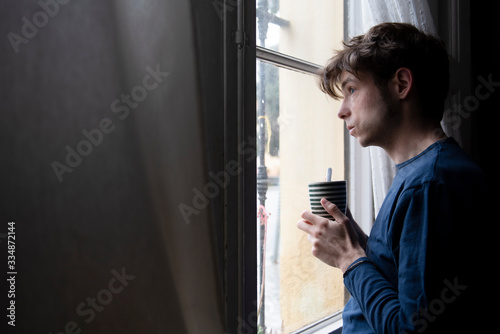 man in pyjamas looking through the window during quarentine