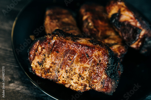 A black plate full of smoked pork chops from an outdoor barbecue grill smoker