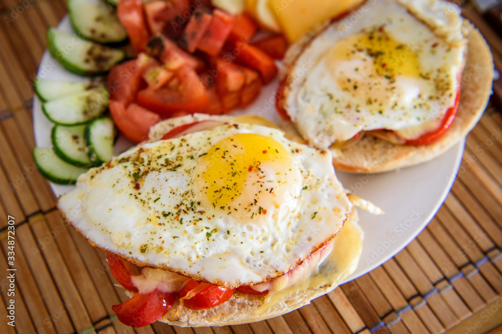 Snippet of a colorful breakfast containing two fried eggs with grilled bell pepper on the toast, and some vegetables on the side arranged on a white ceramic plate on a wooden place-mat. Snippet of a colorful breakfast containing two fried eggs with grilled bell pepper on the toast, and some vegetables on the side arranged on a white ceramic plate on a wooden place-mat.