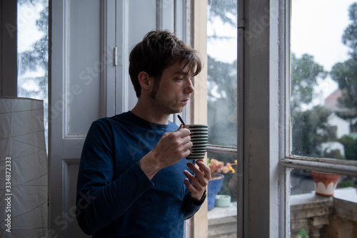 man in pyjamas looking through the window during quarentine photo
