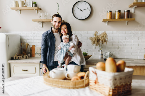 Very happy caucasian family of three in the kitchen of mother, father and baby daughter