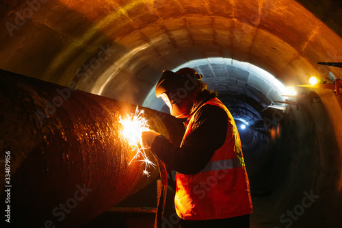 Worker in protective mask welding pipe in tunnel photo