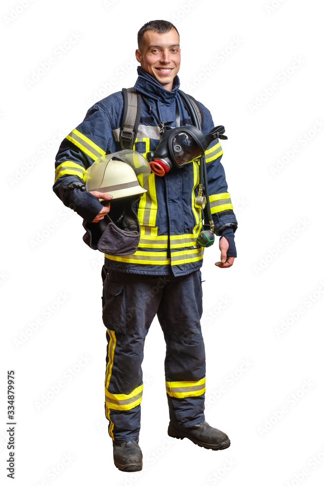 young smiling fireman in a fireproof uniform stands and looks at the camera with a helmet in his hands. young smiling fireman in a fireproof uniform stands and looks at the camera with a helmet in his hands.