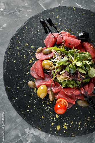 фотографія Beef carpaccio with arugula on a black plate, traditional Italian cuisine
