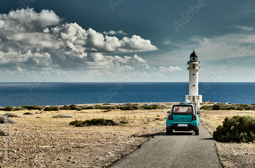 Lighthouse on the Formentera island, Spain, the blue sky with white clouds, without people, car is on a path to lighthouse photo