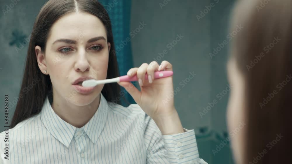 4K Chest-up mirror shot of gorgeous young business woman brushing teeth in bathroom and looking at reflection in mirror. Oral hygiene. Teen girl cleaning 4K Chest-up mirror shot of gorgeous young business woman brushing teeth in bathroom and looking at reflection in mirror. Oral hygiene. Teen girl cleaning