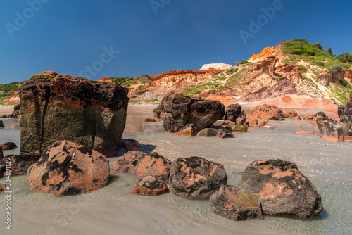 Colored stones and sand on the beach, in the background cliffs with natural vegetation at Praia de Peroba, Icapui, Ceara, Brazil on April 23, 2016 photo