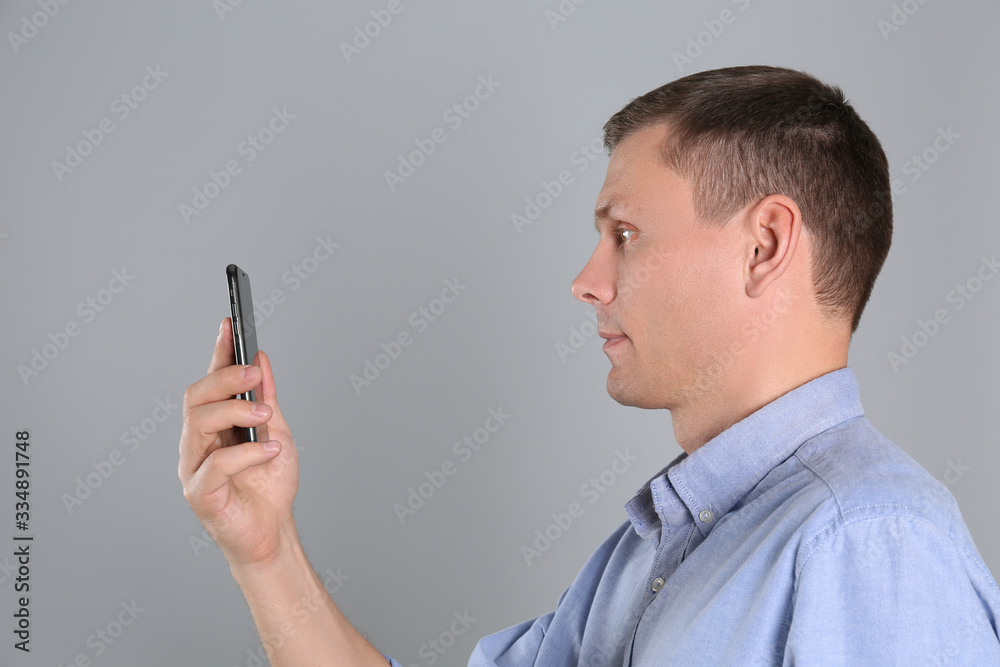 Man unlocking smartphone with facial scanner on grey background. Biometric verification Man unlocking smartphone with facial scanner on grey background. Biometric verification