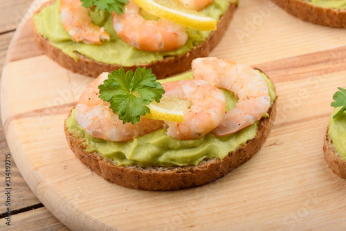 Sandwiches with avocado cream and shrimp on a cutting board.
