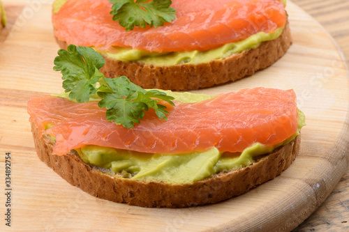 Sandwiches with avocado cream and slices of salmon on a cutting board.