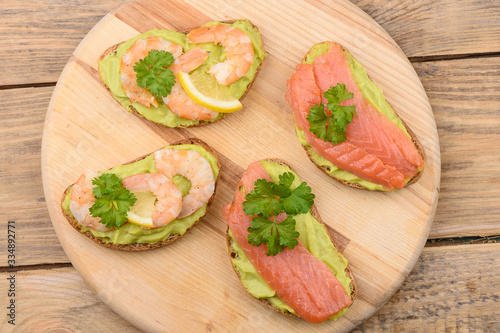 Sandwiches with slices of salmon and shrimp decorated with parsley and lemon.