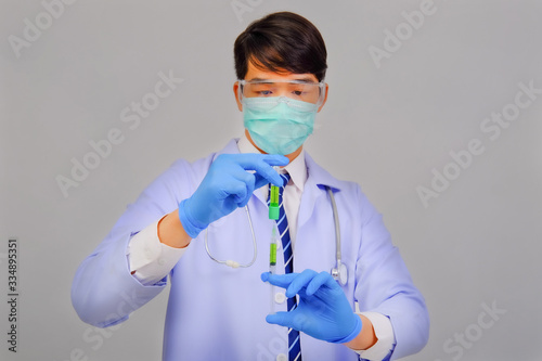 Medical doctor in white uniform doctor wears medical gloves, medical masks and and wearing protective glasses holding vaccine vial on gray background, corona virus concept, medical concept photo