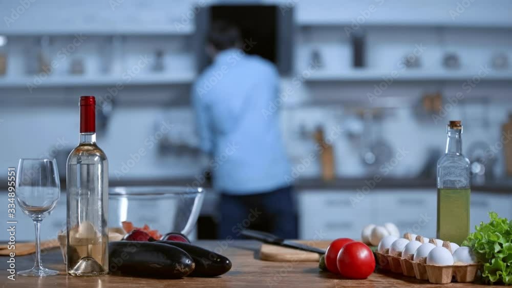 selective focus of fresh vegetables, white wine and oil, and man on background selective focus of fresh vegetables, white wine and oil, and man on background