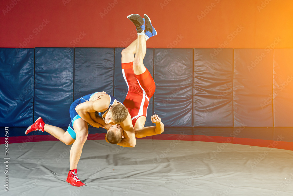 Φωτογραφία Two strong wrestlers in blue and red wrestling tights are wrestlng and making a  making a hip throw  on a yellow wrestling carpet in the gym