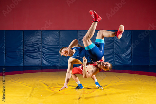 The concept of fair wrestling. Two greco-roman wrestlers in sportwears makes throw through the back on a wrestling carpet in the gym.The concept of male wrestling and resistance
