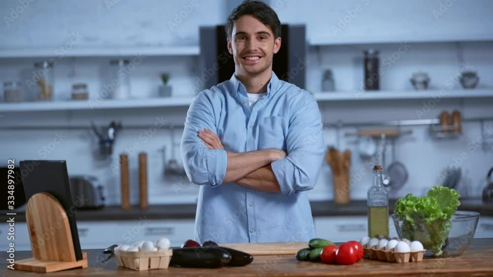 smiling man looking at camera while standing near table with fresh ingredients smiling man looking at camera while standing near table with fresh ingredients