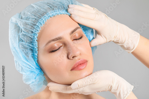 Plastic surgeon examining face of young woman on grey background