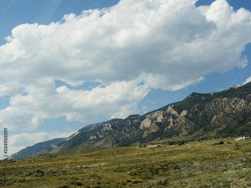 Medium wide shot of mountainside view with thick cotton clouds in the skies along North Fork Highway in Wyoming.