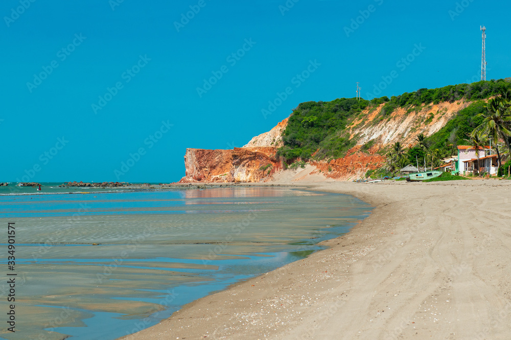 Sunny morning, where you can see boats, houses and the cliff with vegetation in the background in Praia Redonda, Icapui, Ceara, Brazil on April 23, 2016